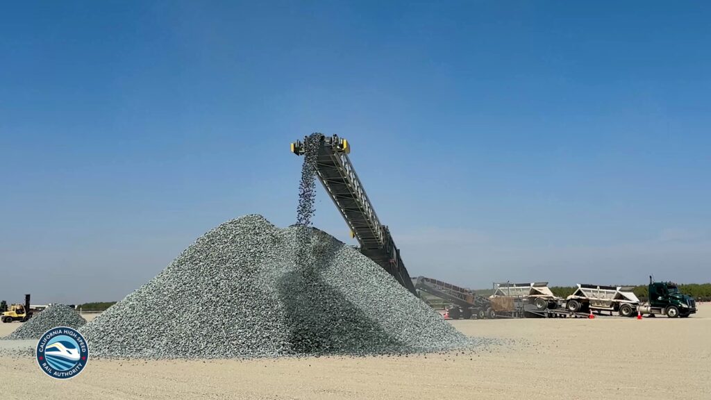Large pile of ballast rock beside a conveyor and trucks at a California High-Speed Rail construction site