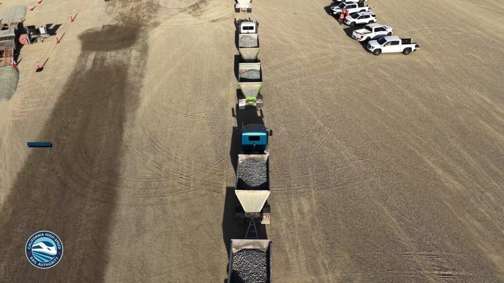 Aerial view of trucks lined up with loads of ballast rock at a California High-Speed Rail construction staging area